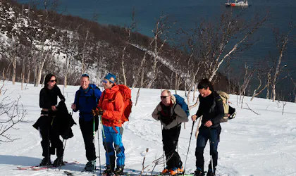 Mennesker på skitur med blått hav i bakgrunnen.