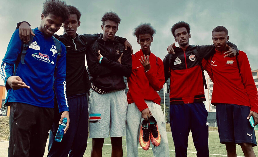 Seks mennesker står tett sammen på fotballbane.